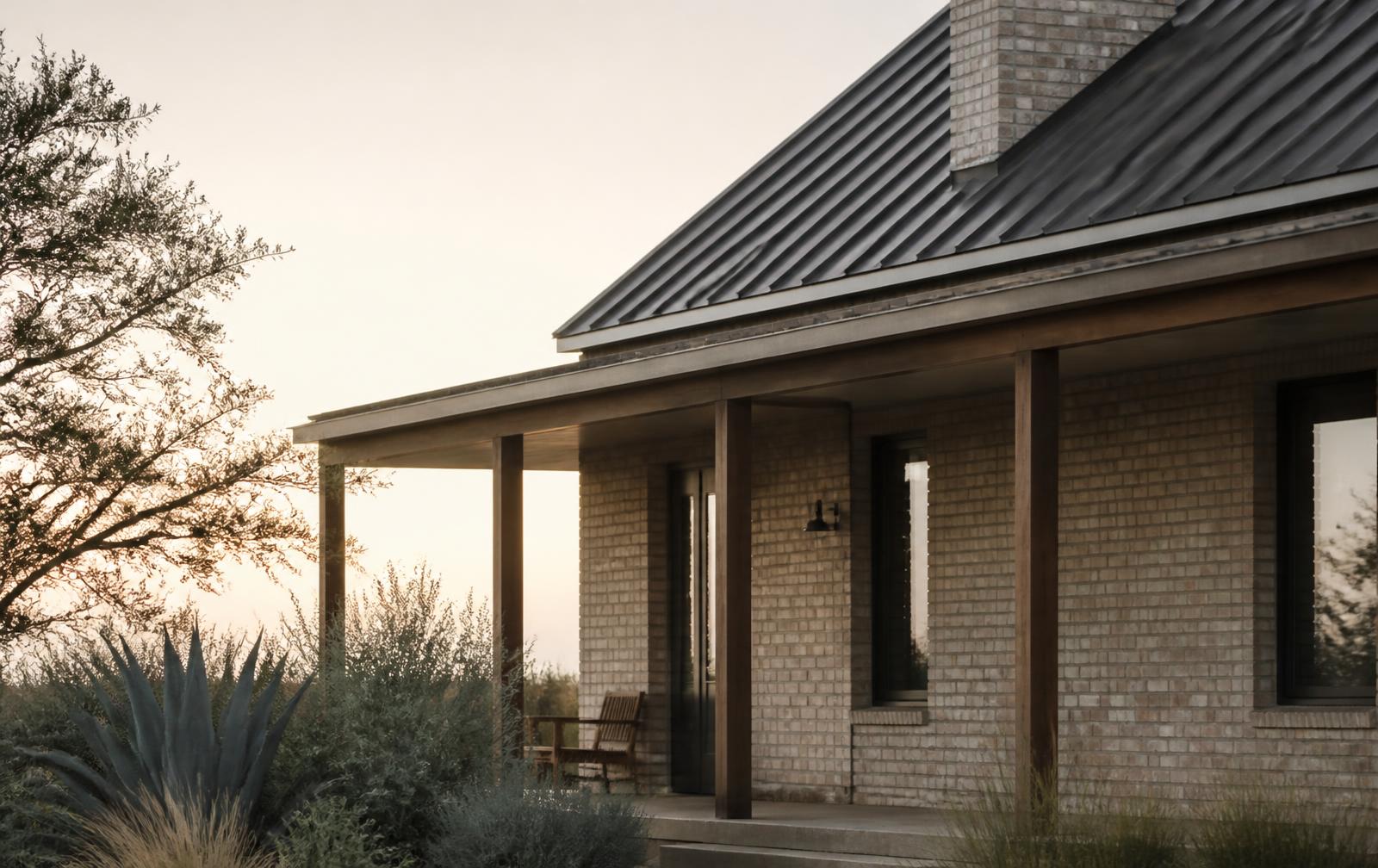 Evening light on the brick facade and covered front porch of a Texas home surrounded by native plantings.